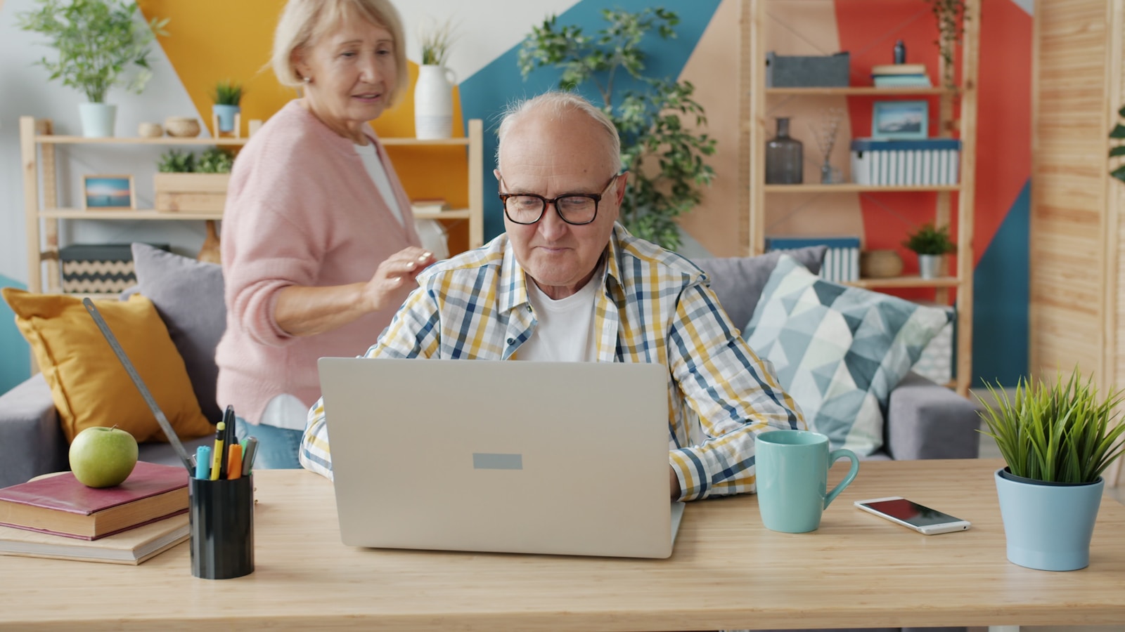Happy retired people man and woman are using computer talking hugging expressing love and care in apartment. Lifestyle, family and devices concept.
